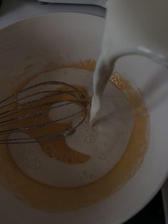 a whisk being poured into a white bowl filled with liquid and other ingredients