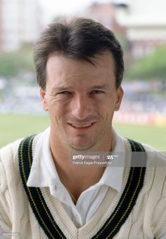 a smiling man wearing a sweater and vest in front of a baseball field stock photo