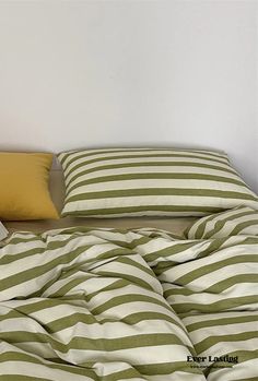 an unmade bed with green and white striped comforter on the bottom, next to two pillows