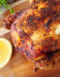 a close up of a chicken on a cutting board with lemon wedges and herbs