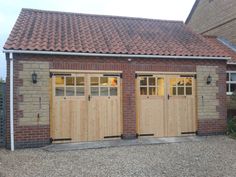 two wooden garage doors are open in front of a brick building with a red tiled roof