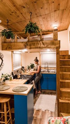 a woman sitting at the kitchen counter in a tiny house with stairs leading up to the loft