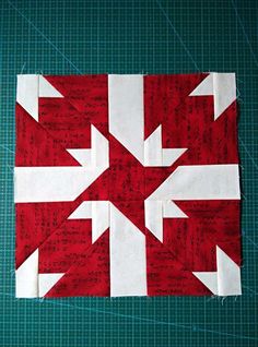 a red and white quilted block with an arrow on the center is sitting on a green surface