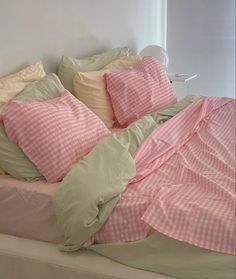 an unmade bed with pink gingham comforter and pillows on the headboard