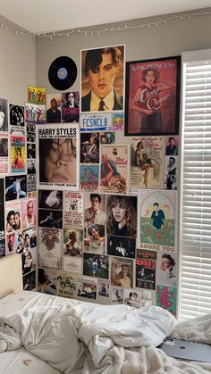 a bedroom with posters on the wall and a white bed in front of a window