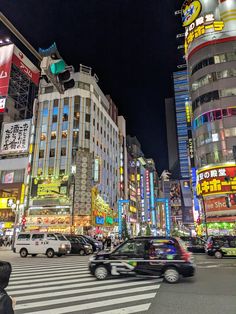 a busy city street at night with cars and people crossing the street in front of tall buildings