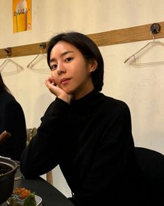 a woman sitting at a table with food in front of her and another person behind her