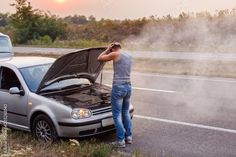 a man standing next to a car with its hood open on the side of the road