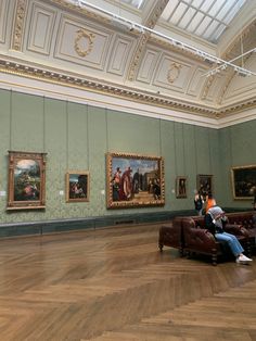 people are sitting on couches in an art gallery with paintings hanging on the walls