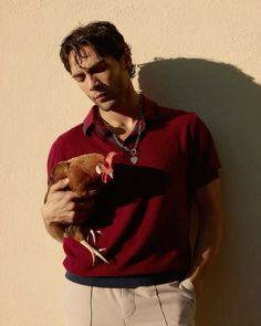 a man in a red shirt holding a brown and white chicken next to a wall