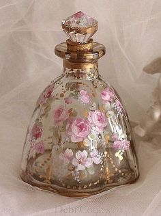 a glass bottle with flowers painted on the top and gold trimmings around it