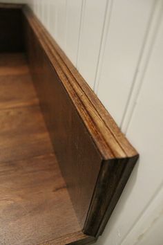 a wooden shelf sitting on the side of a wall next to a white painted wall