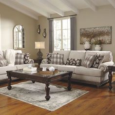 a living room filled with furniture on top of a hard wood floor covered in white and brown pillows