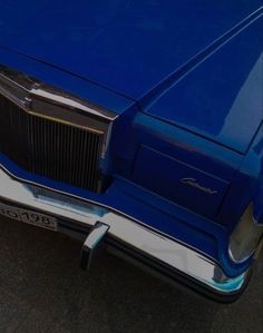 an old blue car parked on the side of the road with its hood up and grilles down