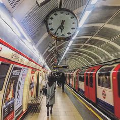 people are walking in the subway station with a clock hanging from the ceiling above them