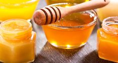 several jars of honey sit next to each other on a table with wooden spoons