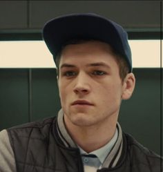 a young man wearing a baseball cap and vest