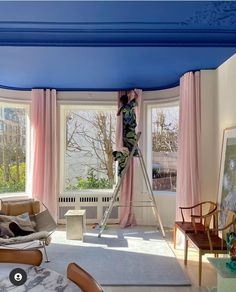 a woman is painting the ceiling in her living room with blue and pink paint on the walls