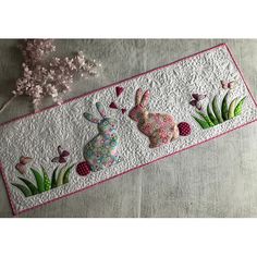 an embroidered table runner with two rabbits on it and pink flowers in the back ground