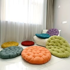 four different colored cushions sitting on the floor in front of a white curtained window