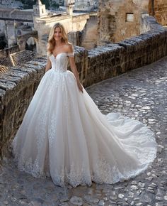 a woman in a white wedding dress standing on a stone wall next to an old city