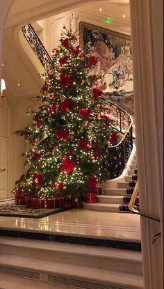 a decorated christmas tree in the middle of a room with stairs and paintings on the walls