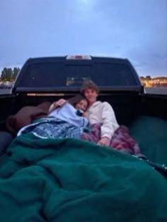 two people laying in the back of a pick up truck with blankets on it's bed