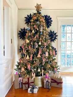 a christmas tree decorated with blue and pink bows in a living room next to two presents