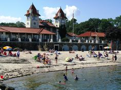 many people are on the beach and in the water near some buildings with brown roofs