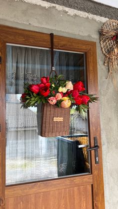 a basket filled with flowers hanging from the side of a wooden door next to a window