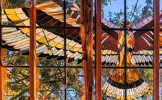 a stained glass window with a bird hanging from it's side and trees in the background