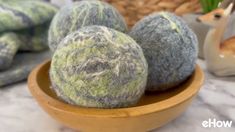 three balls of yarn sitting on top of a wooden bowl next to a basket and potted plant