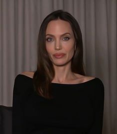 a woman with long hair sitting in a chair and looking at the camera while wearing a black top