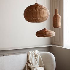 three wicker lamps hanging from the ceiling above a couch with a blanket on it