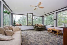 an empty living room with couches, windows and a ceiling fan in the corner