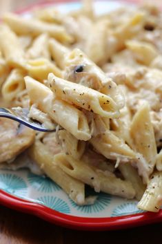 a red and blue plate topped with pasta covered in chicken sauce next to a fork