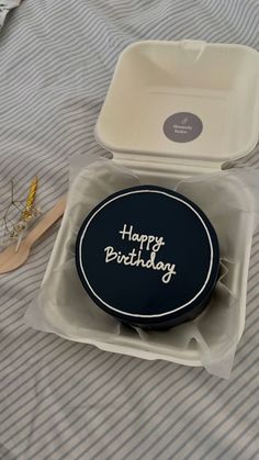 a birthday cake in a box on a bed with a spoon and fork next to it