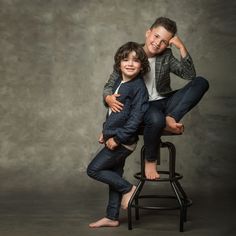 two children sitting on a stool posing for the camera with their arms around each other