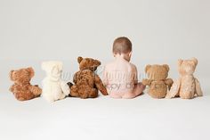 a little boy sitting in front of a row of teddy bears on a white background