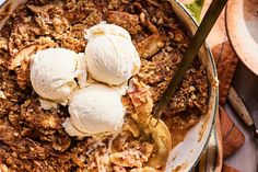 an apple crisp with ice cream on top in a bowl next to two spoons