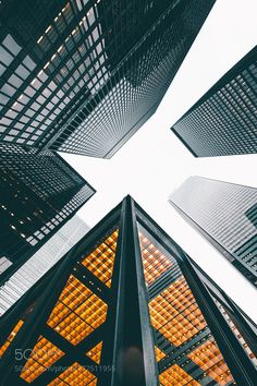 looking up at some tall buildings in the city with yellow lights on them, from ground level