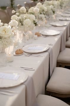 a long table is set with white flowers and place settings for the guests to sit at