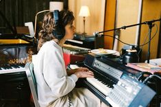 a woman wearing headphones sitting at a piano in front of a microphone and recording equipment