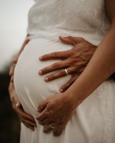 a pregnant woman's hands on the belly of her husband, who is wearing a wedding ring