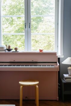 a pink piano sitting in front of a window next to a table with a lamp on it