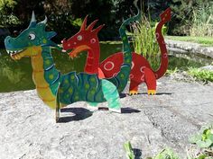 three colorful paper dinosaurs standing on top of a rock next to a body of water