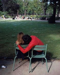 a woman sitting on top of a green chair next to a park filled with trees