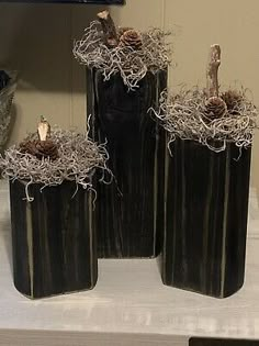 three black vases with pine cones in them sitting on a table next to a mirror