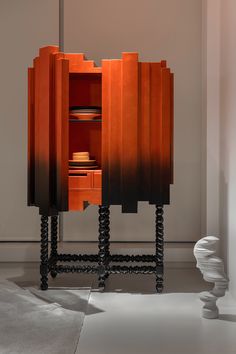 an orange cabinet with black legs and drawers in a white room next to a vase