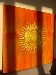 an orange and yellow painting with a sun design on the front, against a white wall